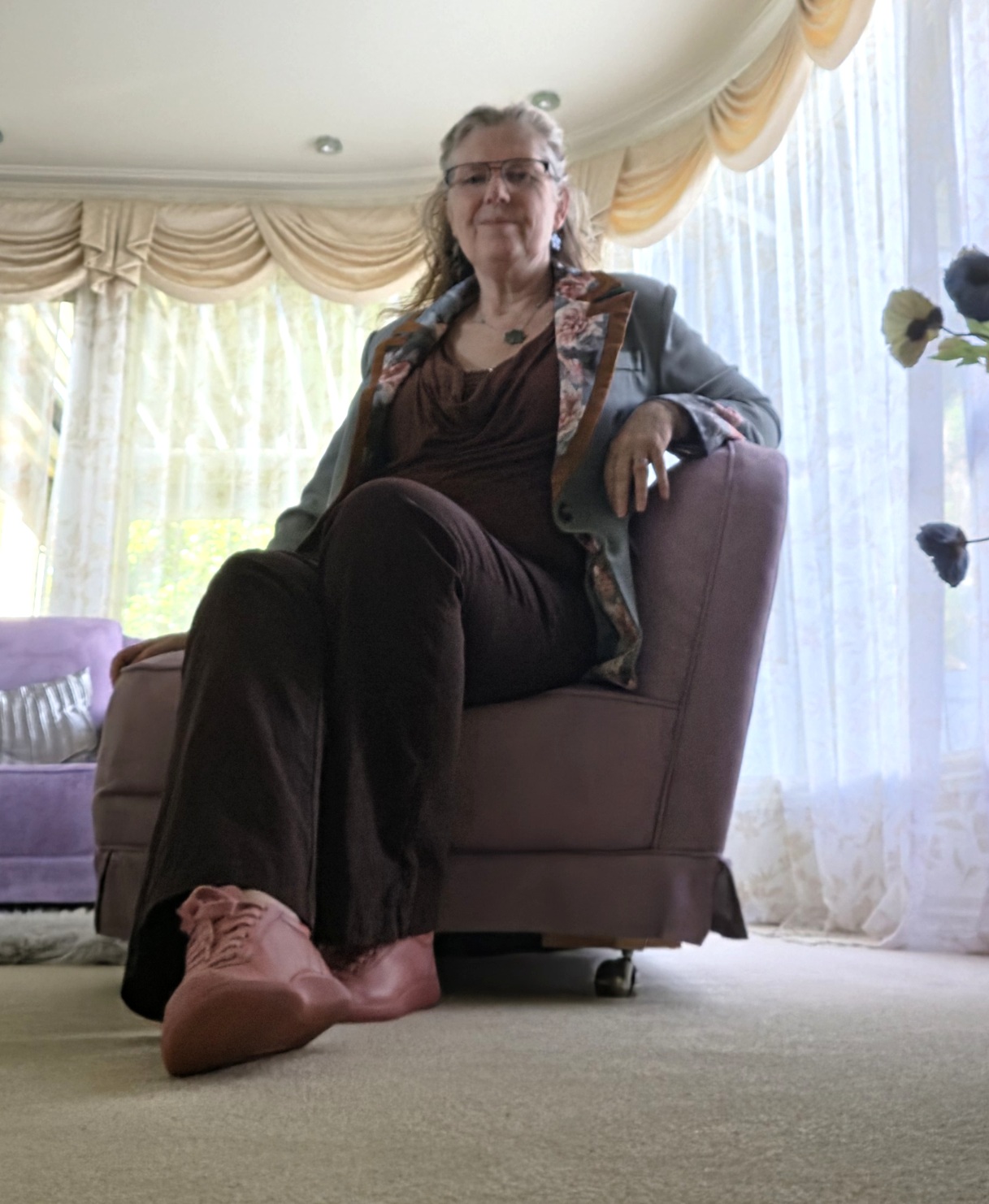 Tania seated at home in her concert outfit: a blue-grey floral-trim jacket, brown top, dark trousers and pink shoes.