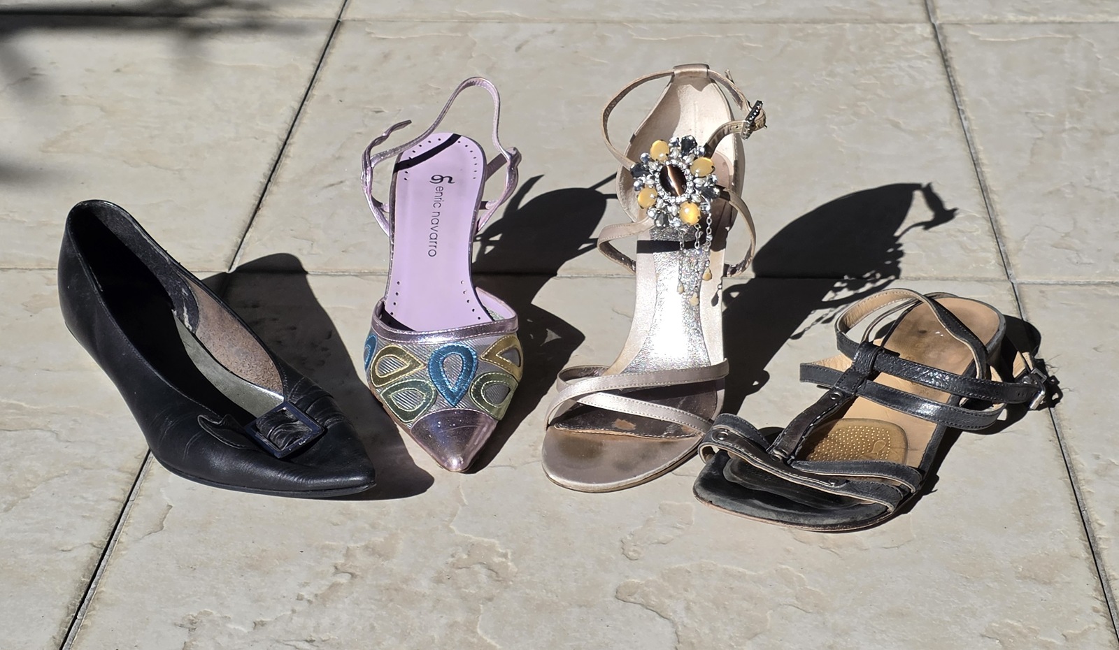 Four of Tania’s favourite shoes on paving: a black pointed shoe, a colourful lilac slingback, a champagne jewelled stiletto and a dark blue sandal.