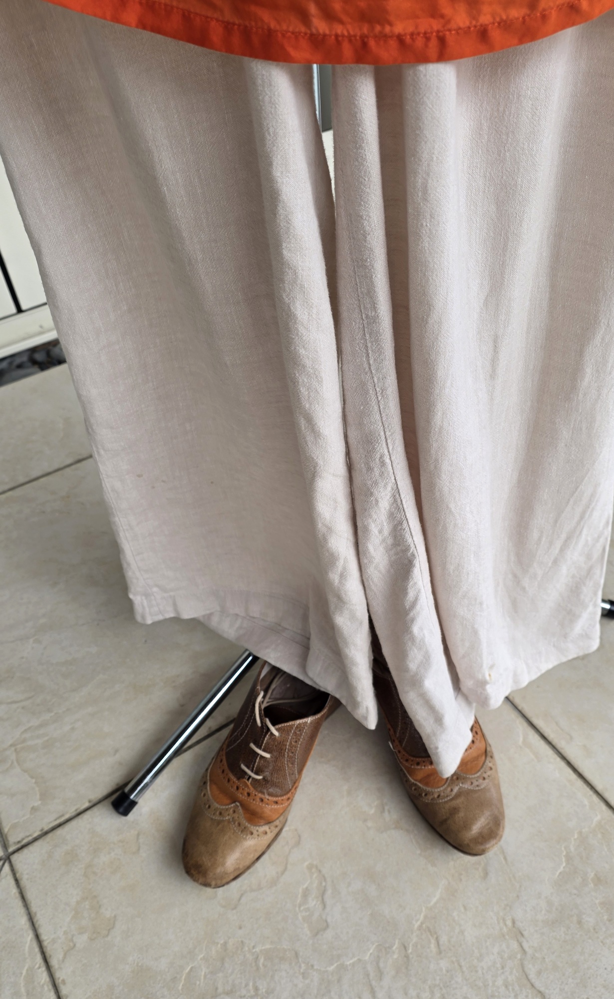 A close-up of pale linen trouser hems and two-tone brown lace-up shoes
