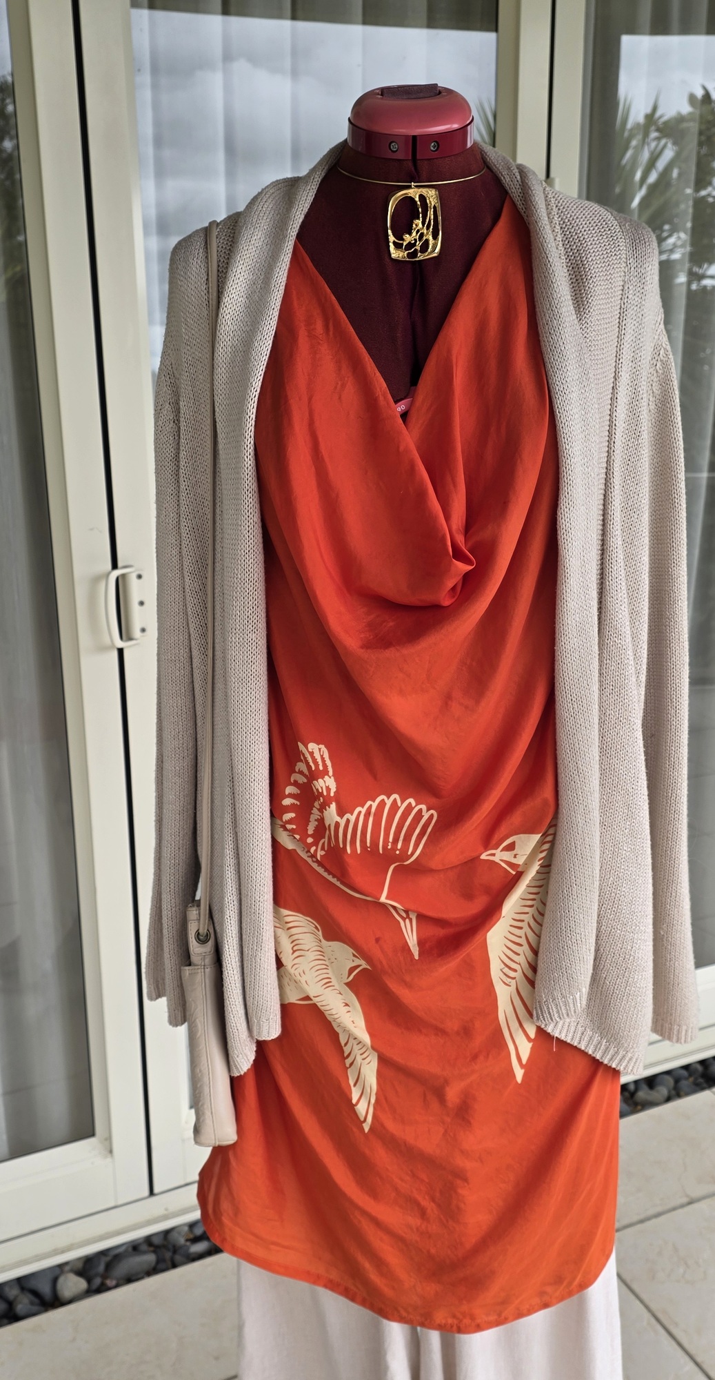 Close-up of the orange silk top's draped neckline, gold pendant and softly textured neutral cardigan.