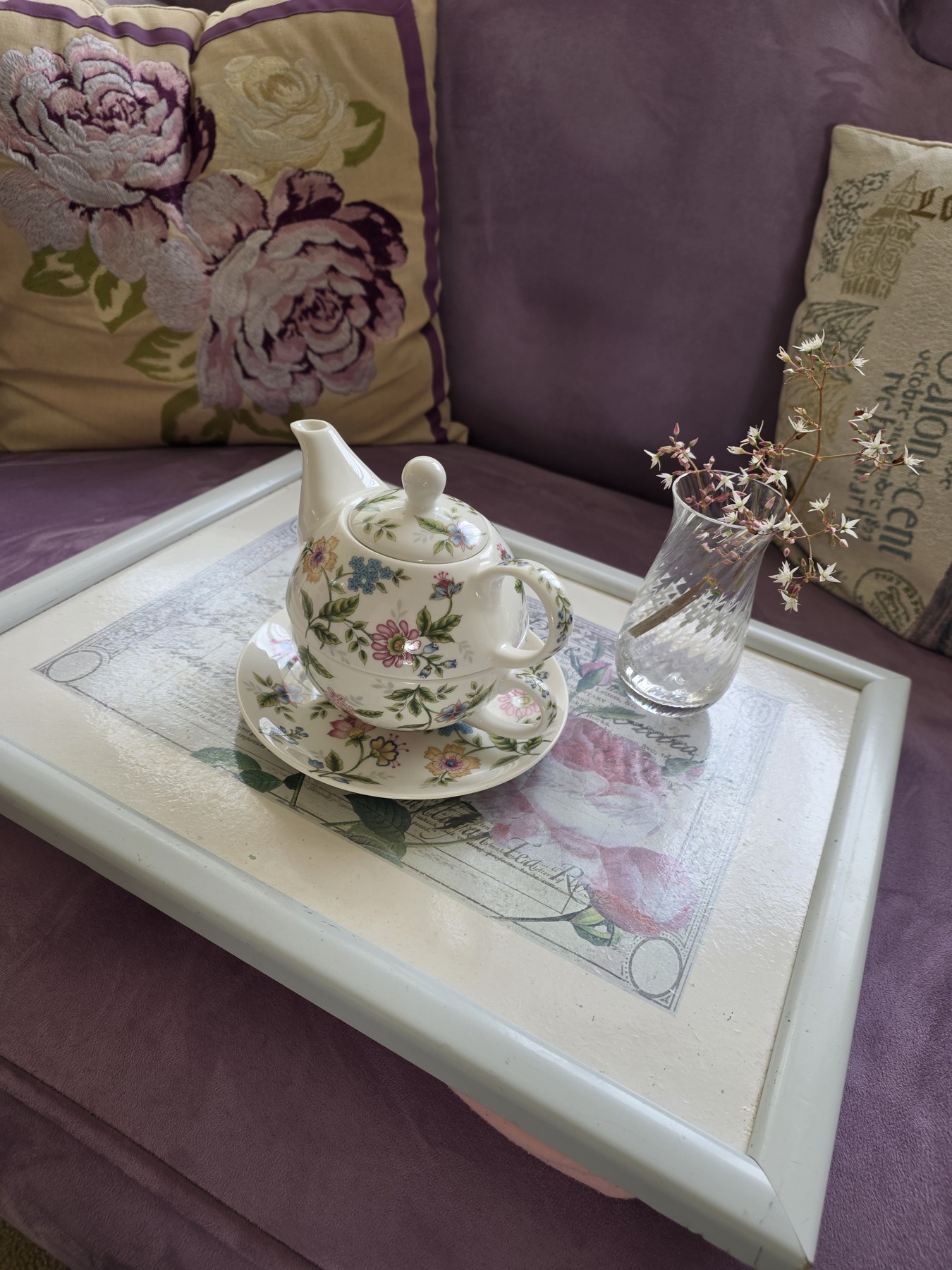 A floral tea-for-one set and a crystal vase of wild garden flowers on a rose-decorated tray, resting on a plum Art Deco chaise