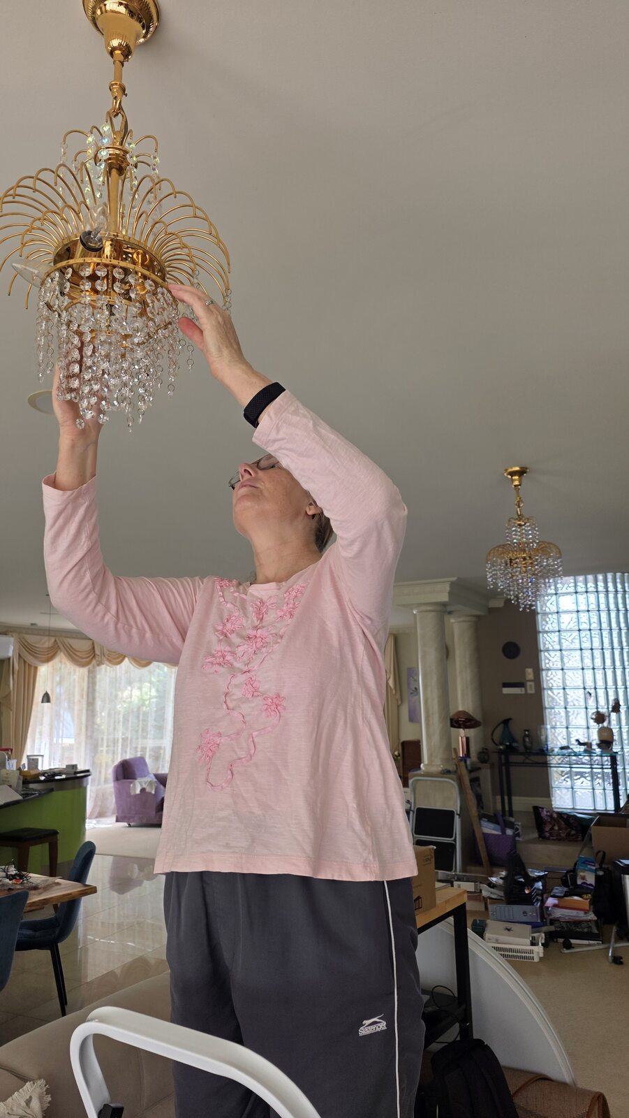 Tania wearing a pink embroidered top and track pants while putting crystals back onto a chandelier