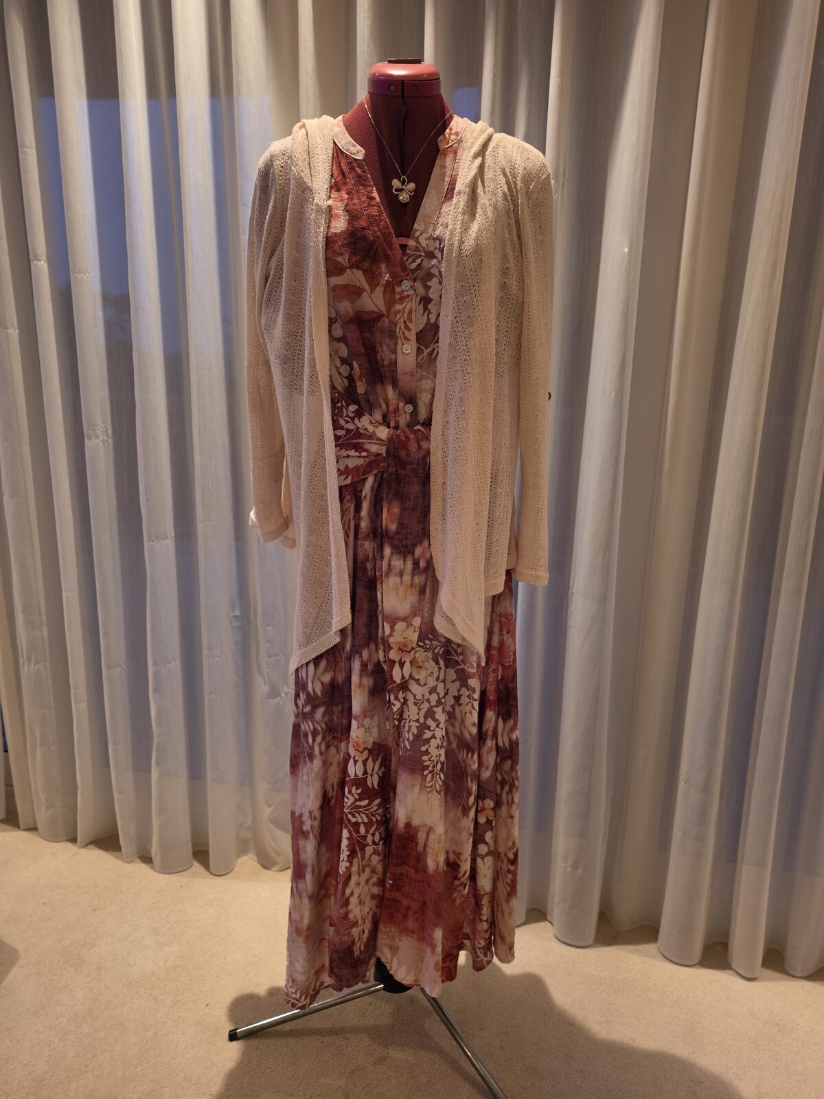A floral dress on a dress form with a soft cream cardigan and a pendant necklace