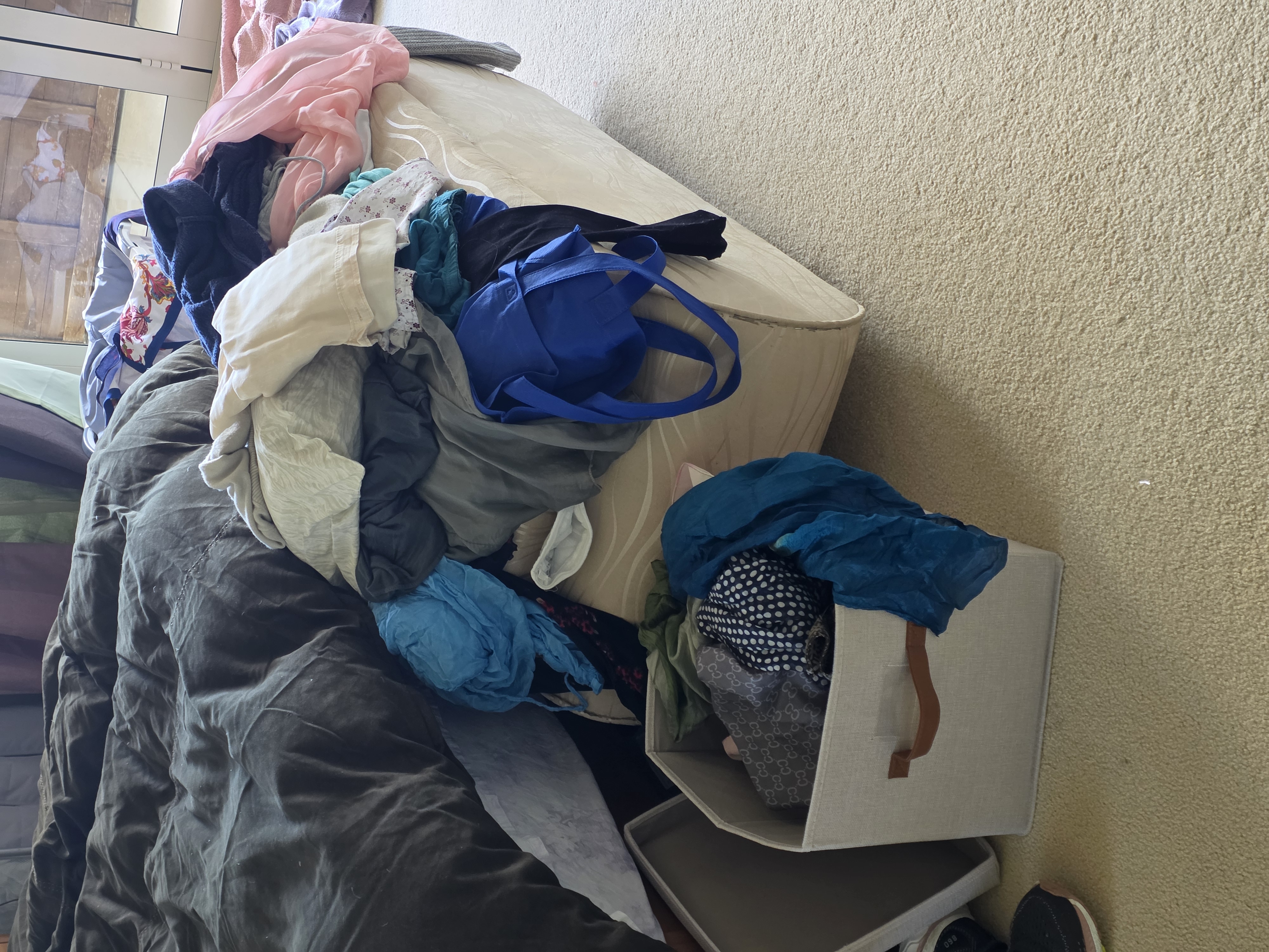 Shirts and tops spread across a bed during wardrobe sorting